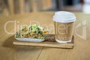 Food and disposable coffee cup on wooden table in cafe
