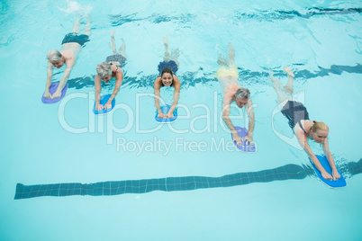 Senior swimmers and trainer swimming with kickboards in pool