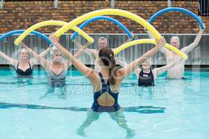 Instructor and senior swimmers exercising with pool noodle