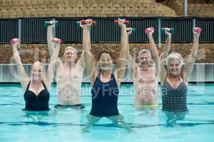 Trainer and senior swimmers lifting dumbbells in swimming pool