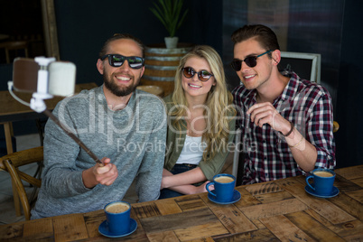 Happy friends taking selfie with monopod in coffee shop