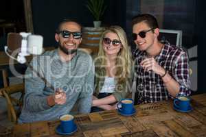 Happy friends taking selfie with monopod in coffee shop