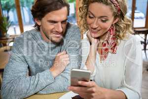 Smiling couple using mobile phone at table in cafe