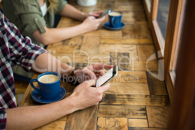 Man and woman using mobile phones in coffee shop
