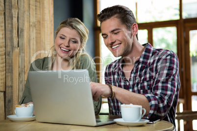 Cheerful couple using laptop at table in coffee shop