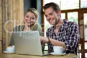 Cheerful couple using laptop at table in coffee shop