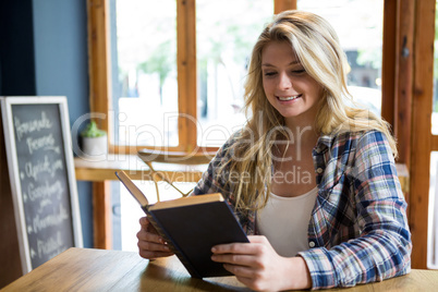 Smiling woman reading book at table in coffee shop