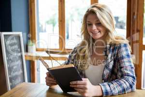 Smiling woman reading book at table in coffee shop