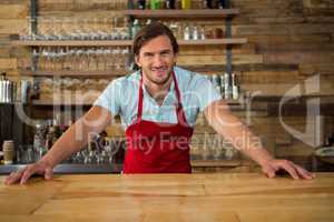 Smiling young male barista at counter in coffee shop