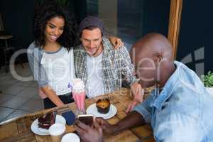 Man showing cell phone to couple at table in coffee shop