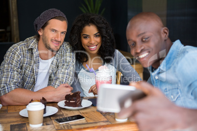 Man with friends taking selfie at wooden table in coffee shop