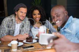 Man with friends taking selfie at wooden table in coffee shop
