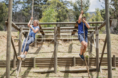 Fit man and woman climbing down the rope during obstacle course