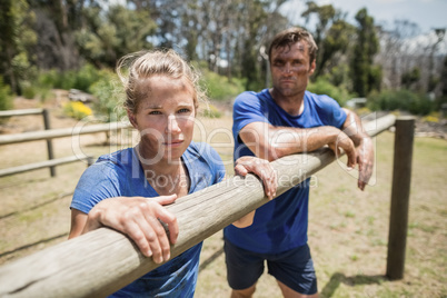 Tired man and woman leaning on a hurdle during obstacle course