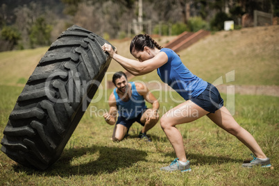 Fit woman flipping a tire while trainer cheering during obstacle course