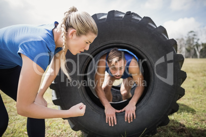Man crawling through the tire during obstacle course while trainer cheering