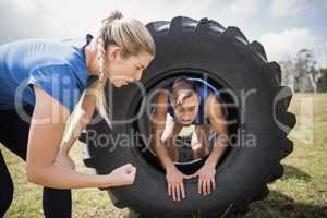 Man crawling through the tire during obstacle course while trainer cheering