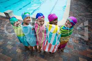 Rear view of little swimmers wrapped in towels at poolside