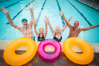 Cheerful senior swimmers with inflatable rings at poolside