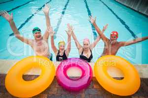Cheerful senior swimmers with inflatable rings at poolside