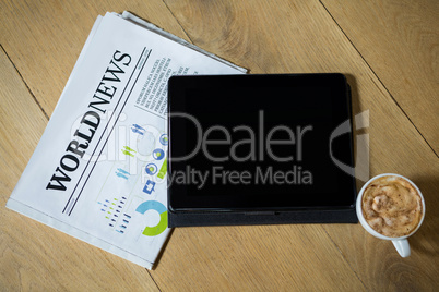 Digital tablet with coffee and newspaper on table in cafe