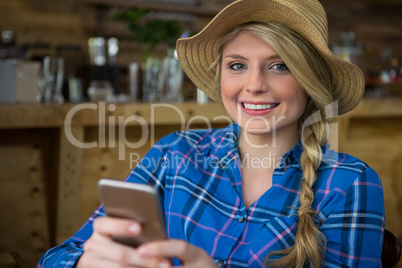 Portrait of smiling woman wearing hat while using mobile phone in coffee shop