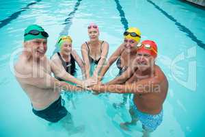 Cheerful senior swimmer stacking hands in pool