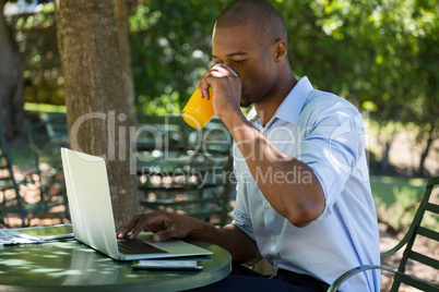 Man drinking juice while using laptop at restaurant