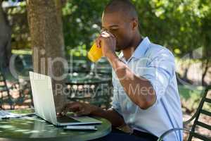 Man drinking juice while using laptop at restaurant