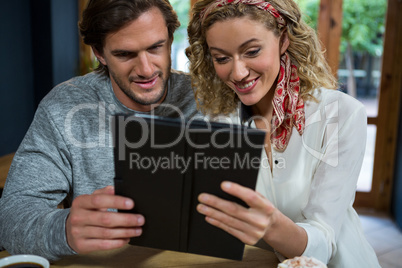 Young couple using tablet computer at table in cafeteria