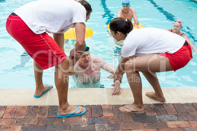 Lifeguards helping unconscious senior man in swimming pool
