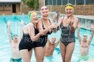 Senior female swimmers holding trophy at poolside