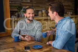 Smiling man talking with friend at table in coffee shop