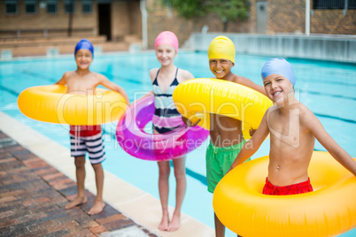 Friends carrying inflatable rings at poolside