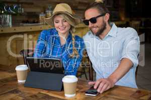 Smiling couple using tablet PC at table in cafeteria