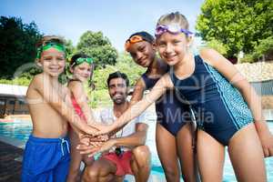 Male instructor and children stacking hands at poolside