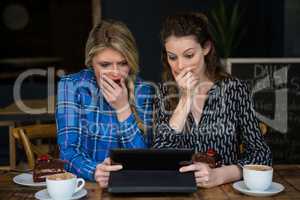 Shocked women using tablet computer in coffee shop