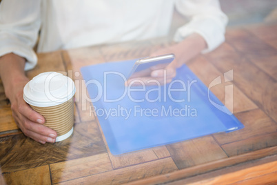 Woman holding coffee cup and smart phone seen through cafe window