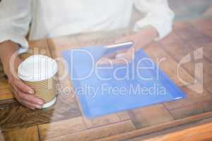 Woman holding coffee cup and smart phone seen through cafe window