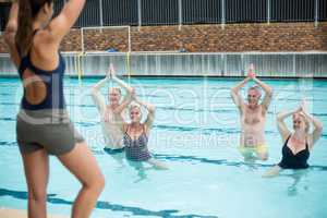 Female yoga trainer assisting senior swimmers at poolside