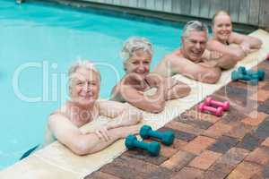 Swimmers leaning by dumbbells at poolside
