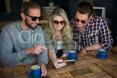 Smiling friends using smart phone at table in cafe