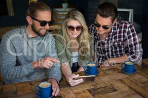 Smiling friends using smart phone at table in cafe