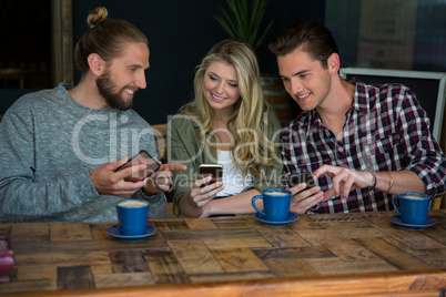 Smiling friends using smart phones at table in cafeteria