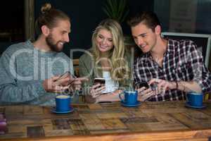 Smiling friends using smart phones at table in cafeteria