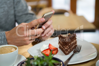 Man using mobile phone with coffee and dessert on table in cafe
