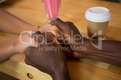 Multi ethnic couple holding hands in coffee shop