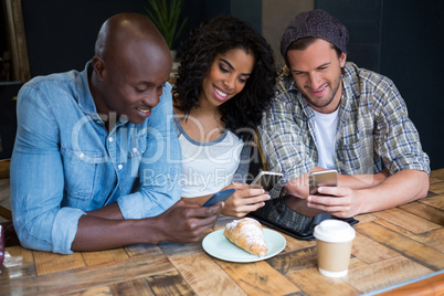 Smiling friends using smart phones at table in coffee shop