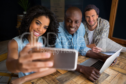 Happy friends taking selfie at wooden table in coffee shop