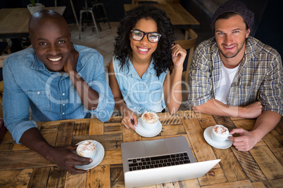 Happy friends having coffee with laptop on table in cafe